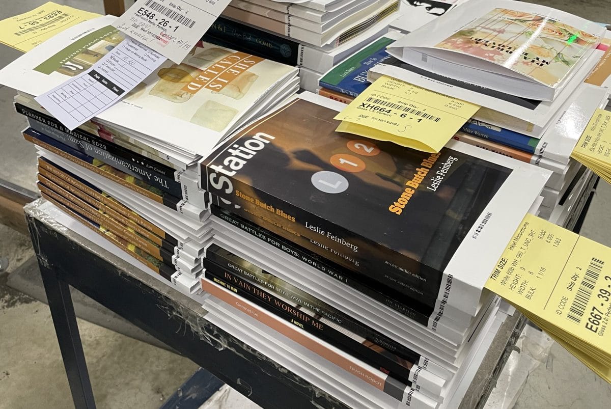 A stack of book blocks matched up with their paperback covers, waiting to have the covers attached. There are a few Lulu books here, including Stone Butch Blues by Leslie Feinberg!