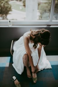 Bride sits in chair wearing sustainable wedding dress from Fame & Partners and puts on handmade clogs by Maguba.