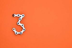 Numerical Three made from bike chain on vibrant orange background
